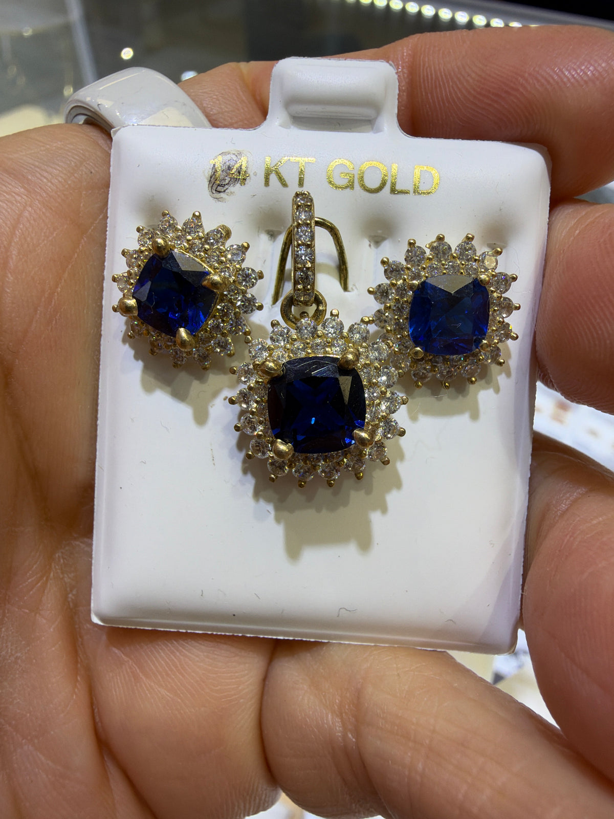 14k Earring and pendant in blue gems set in a floral-inspired sunburst halo design consisting of an inner ring of smaller round accents and an outer scalloped border of marquise-shaped